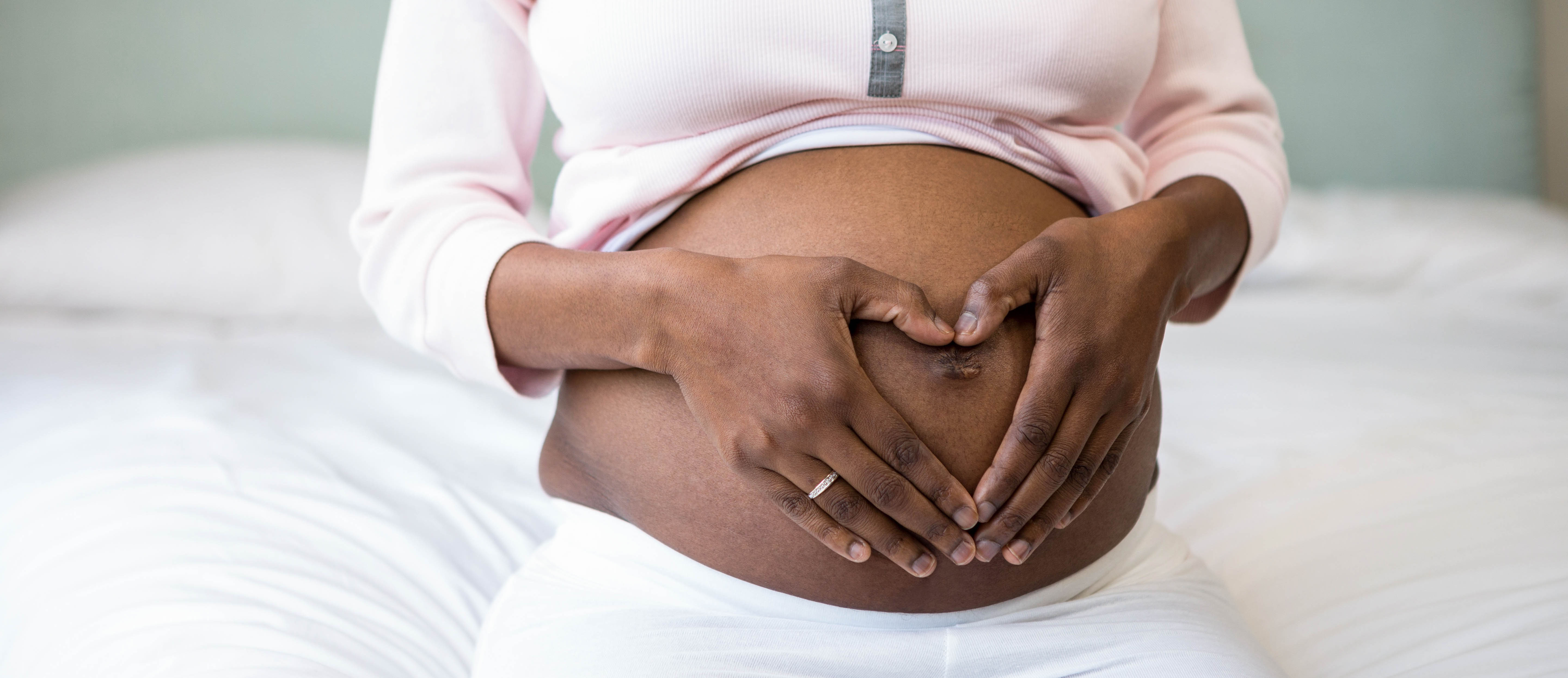 a photo of a black pregnant woman with her hands on her belly forming a heart