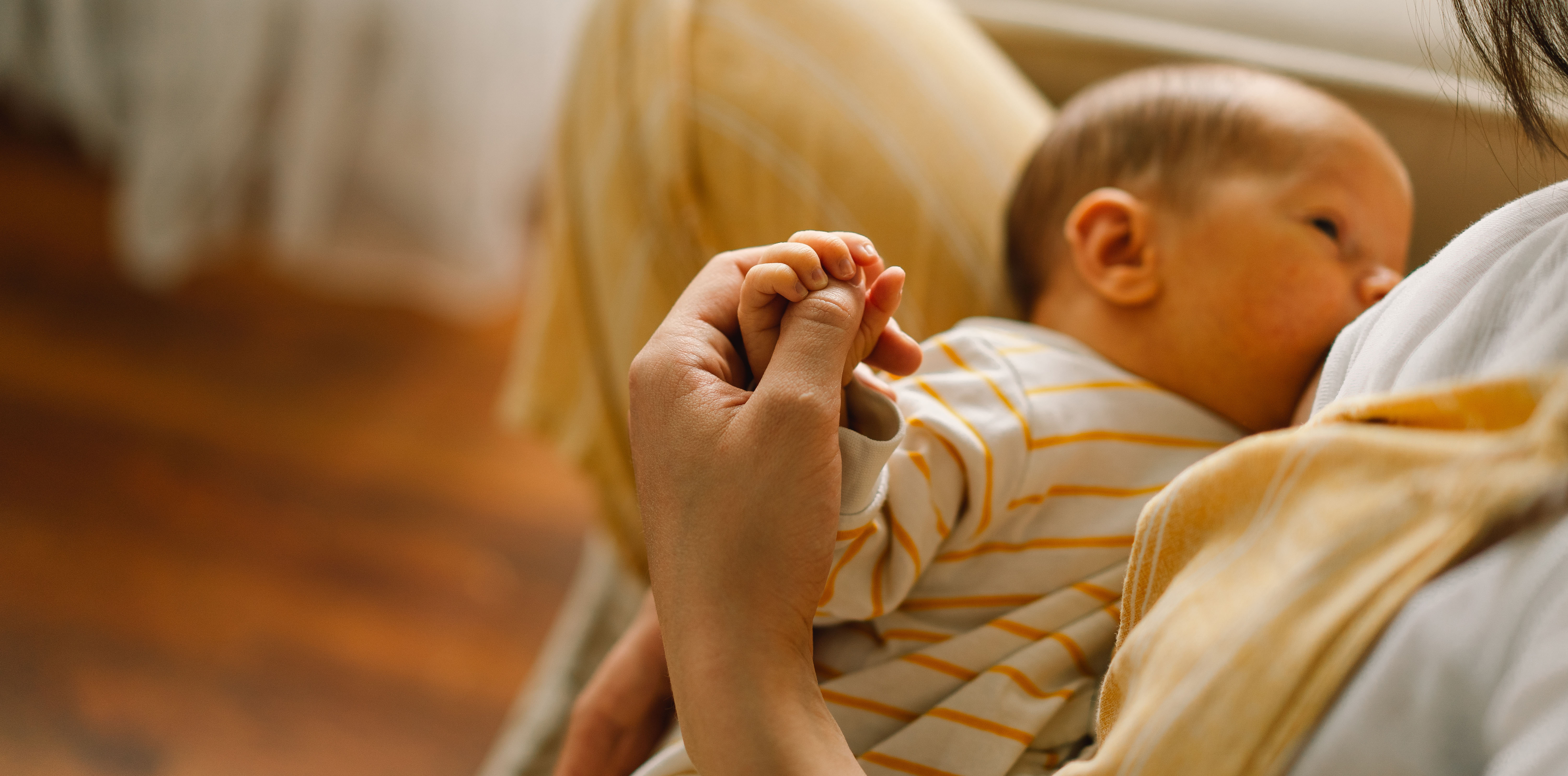 a photo of a woman breastfeeding, holding the hand of her baby