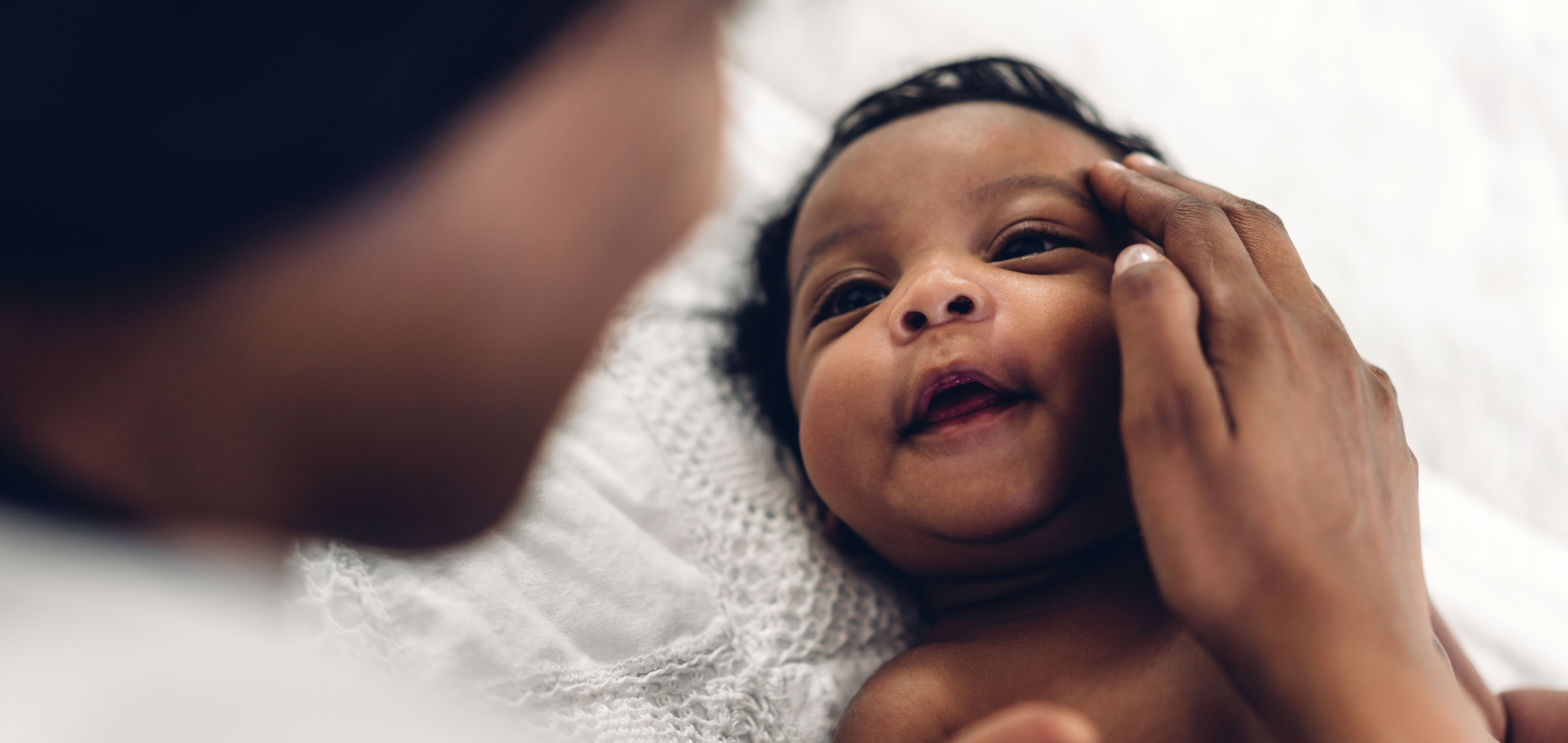 a photo of a small Black baby smiling up at his mom as she touches his face with her hand