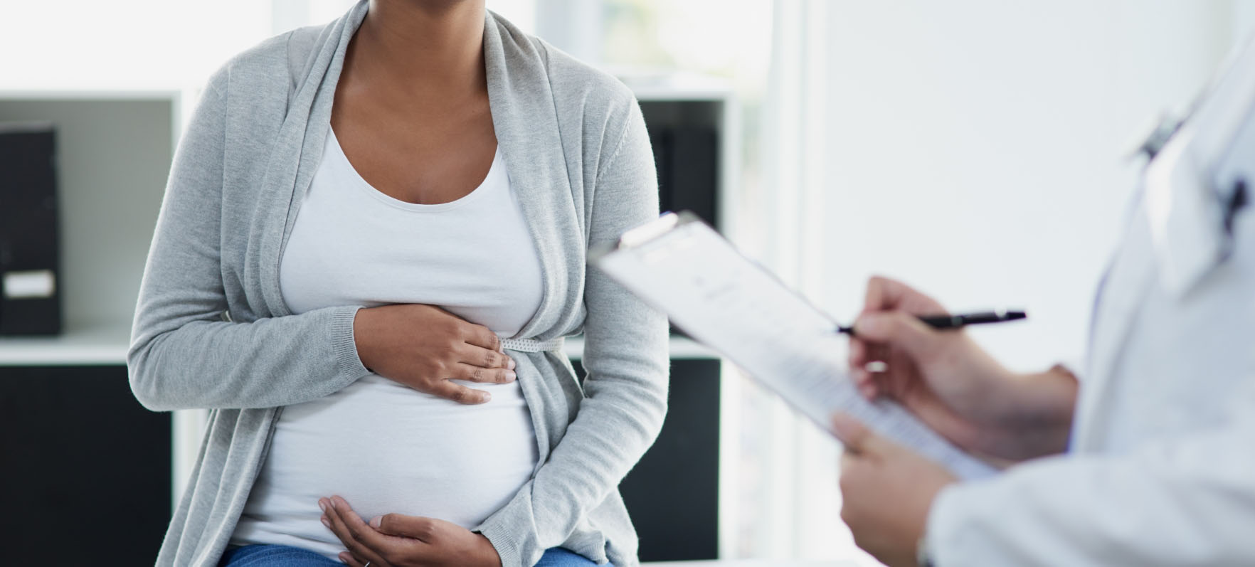 A photo of a pregnant woman sitting in front of her physician