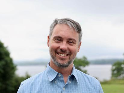 Photo of a man with gray hair smiling with water in the background