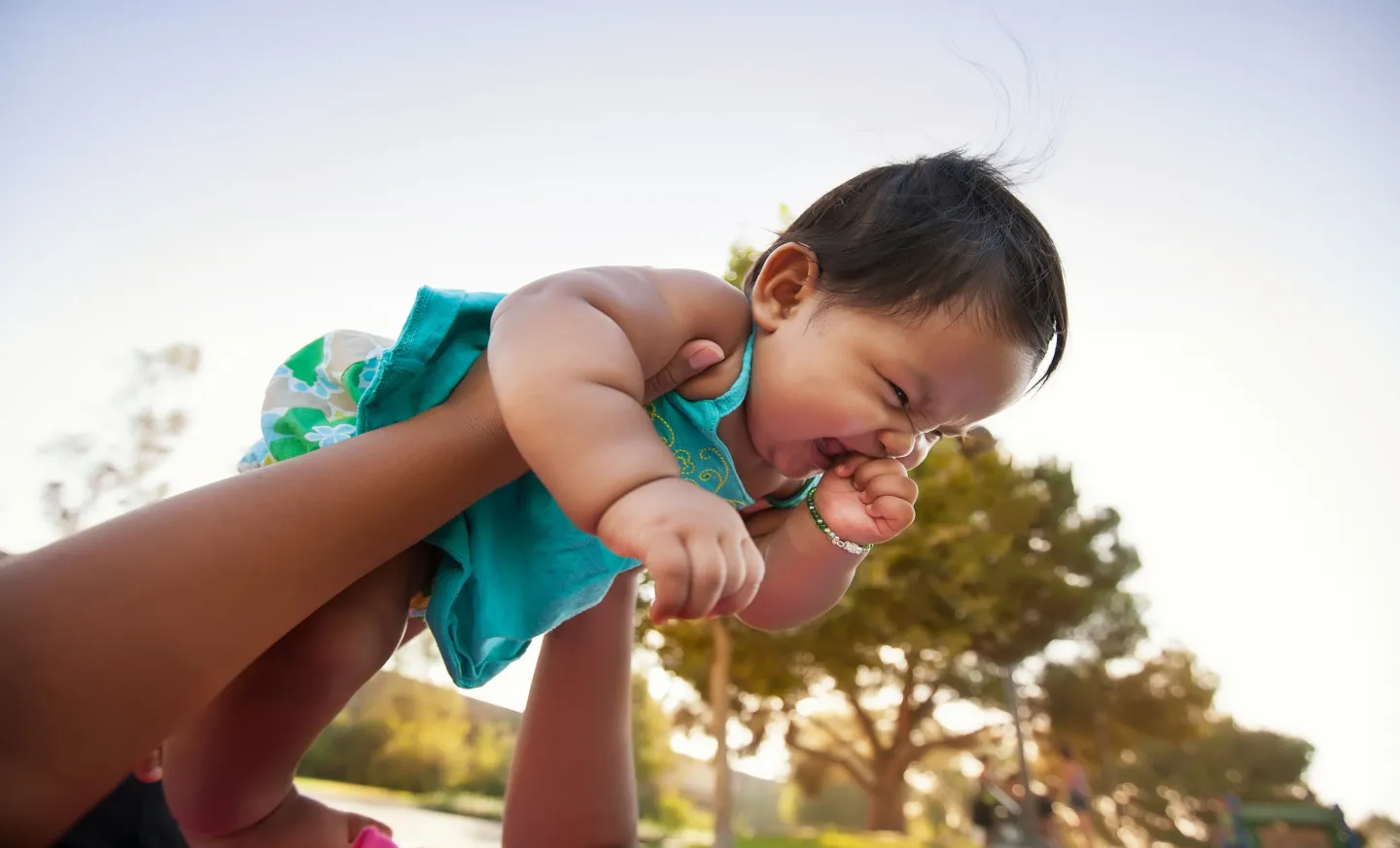 a photo of a young toddler being lifted into the air by her parents and smiling