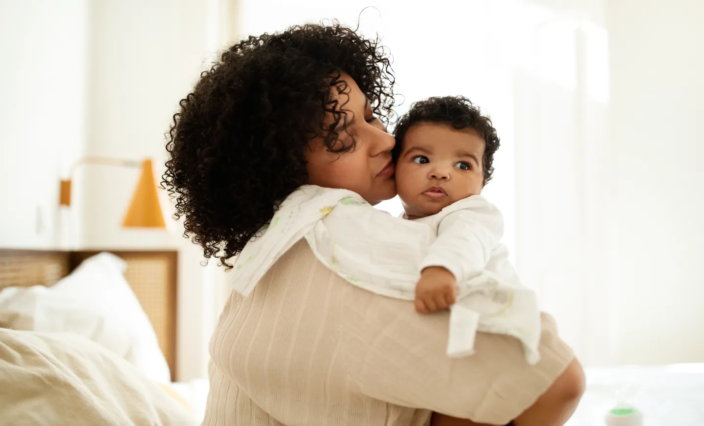 A new mom holds her baby in her arms with a cloth on her shoulder, her face on his cheek