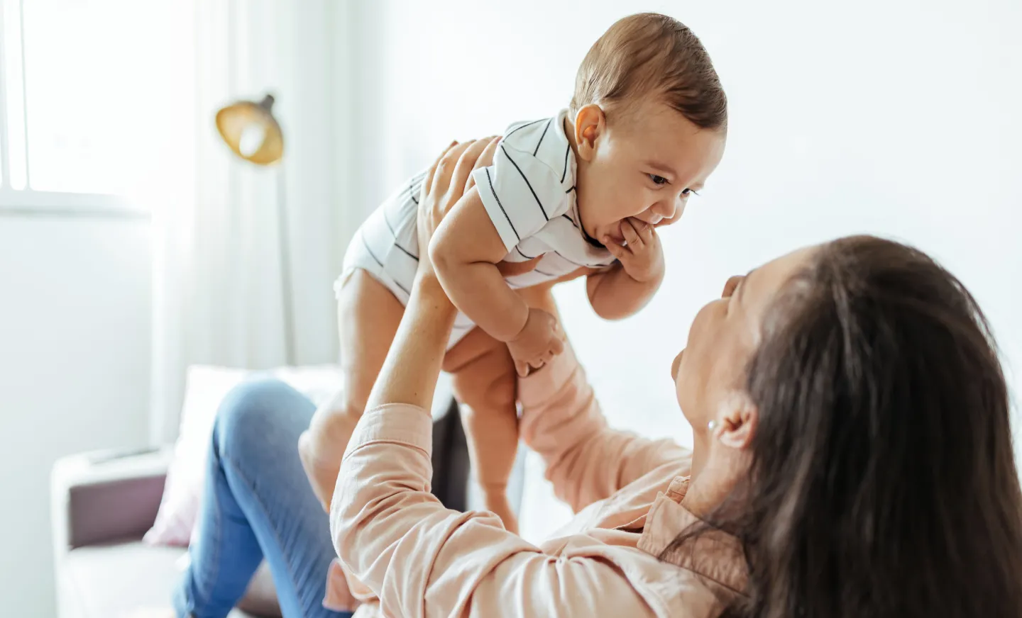 A mom holds her new smiling baby in the air 